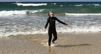 Happy girl in wetsuit coming out of sea on sunny day