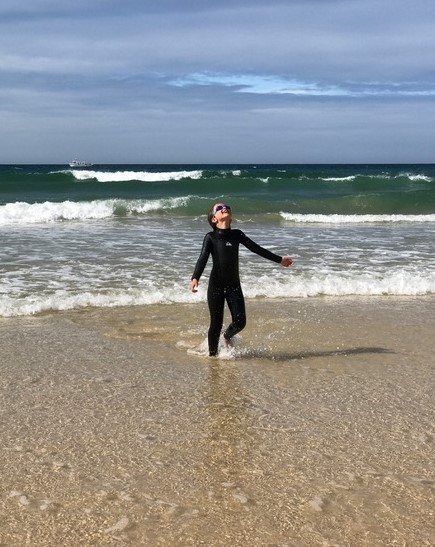 Happy girl in wetsuit coming out of sea on sunny day