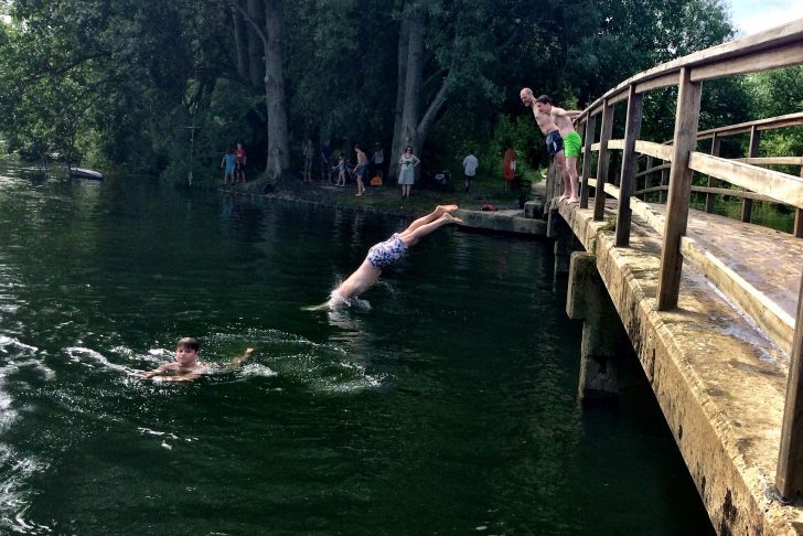 Boys diving off bridge into river on hot day with onlookers