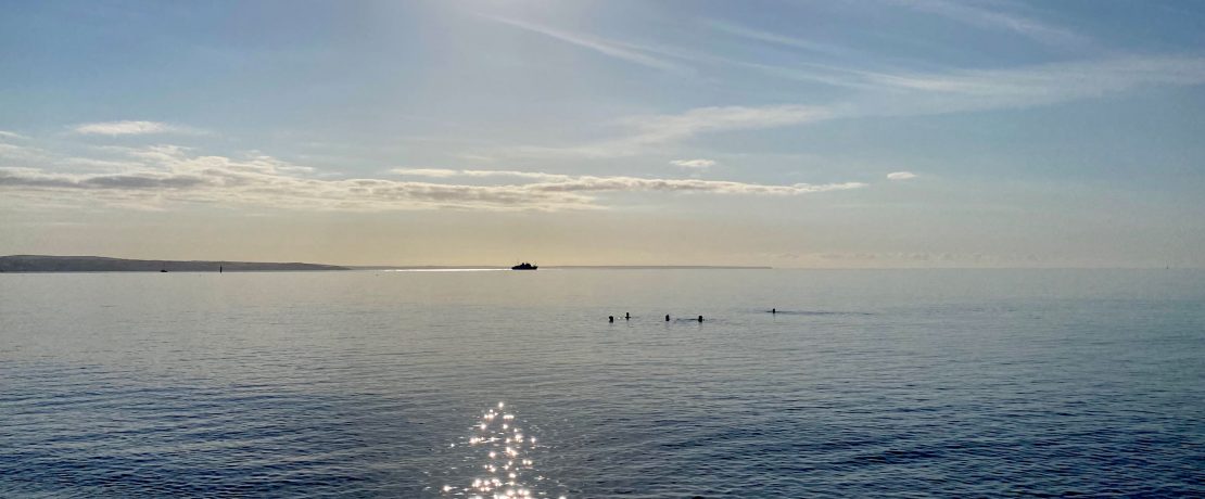 Swimmers out in a bright sea with a boat further out