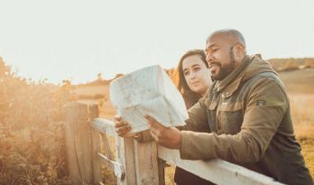 A man and woman lean on a stile and read a map in warm autumn light