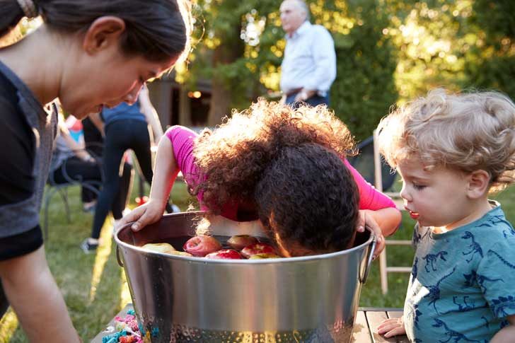 Three children with one plunging face into metal bucket with floating apples