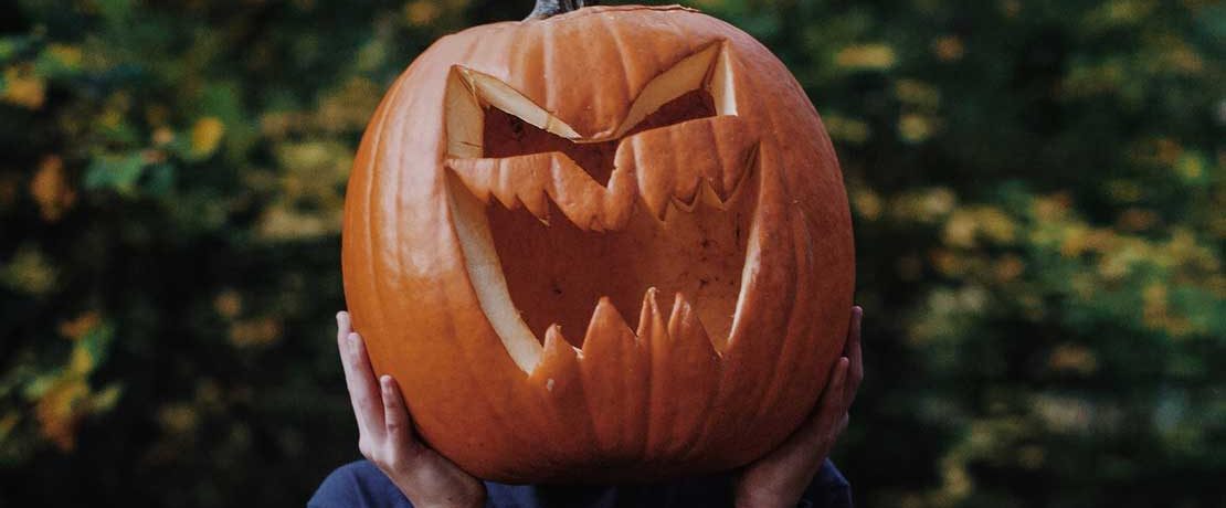 A person holds a large carved pumpkin over their head