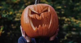 A person holds a large carved pumpkin over their head