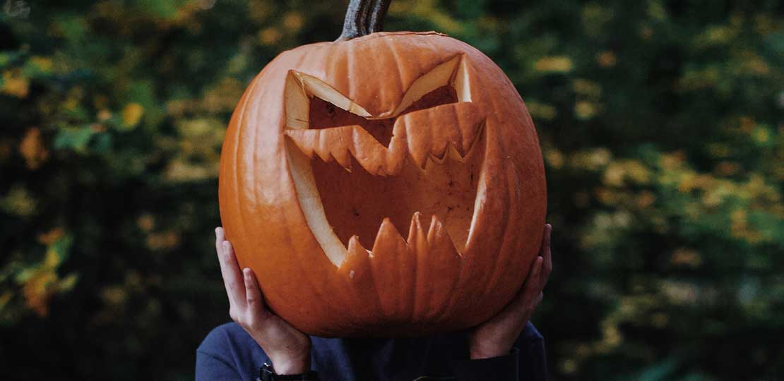 A person holds a large carved pumpkin over their head