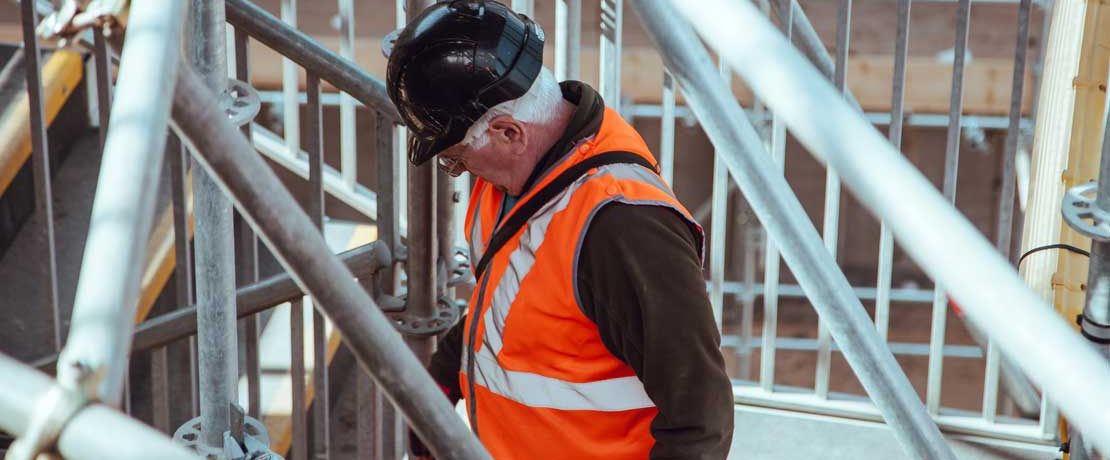 A man with white hair wearing hard hat and high vis jacket on scaffolding