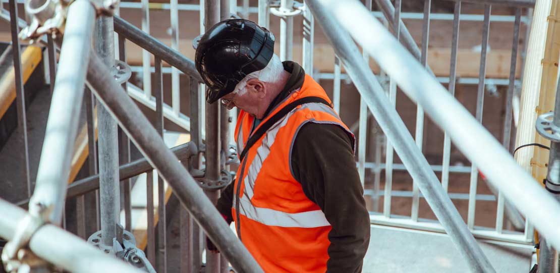 A man with white hair wearing hard hat and high vis jacket on scaffolding