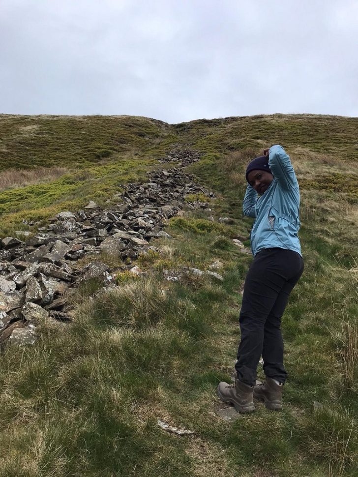 a black woman climbing up a hill on a footpath alongside a stone wall