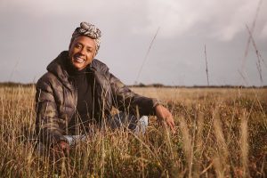 A black woman crouching in a field of long brown grass