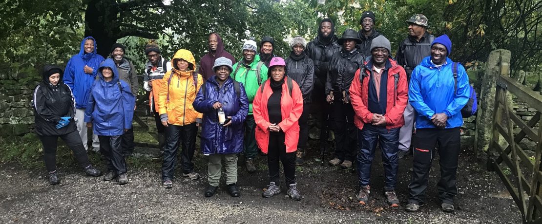 A group of black men and women wearing colourful raincoats standing in a line under trees