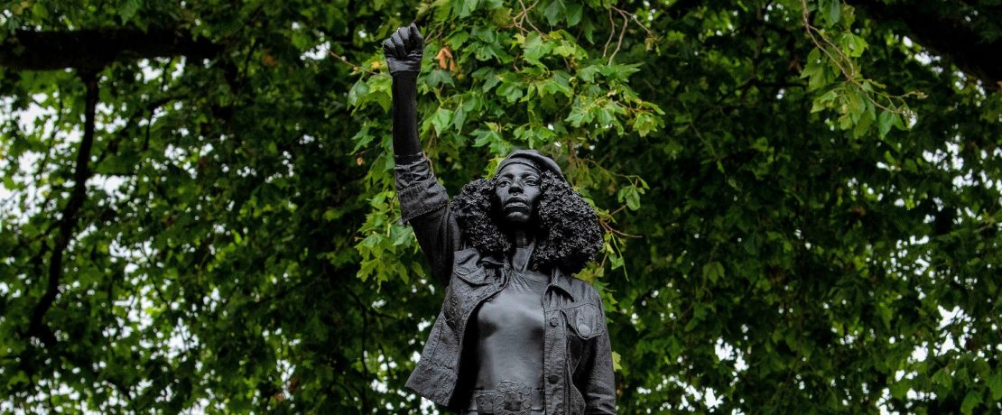 A statue of a black woman with a raised fist surrounded by trees