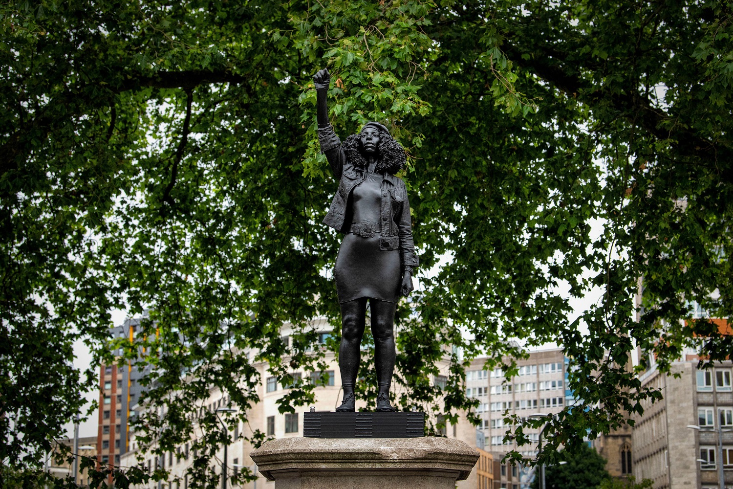 A statue of a black woman with a raised fist surrounded by trees