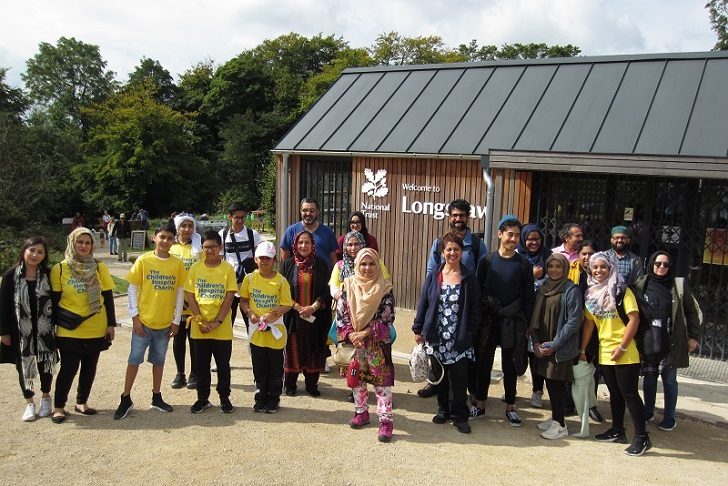 A group of Asian men, men and children standing outside a National Trust visitor centre with countryside in the background