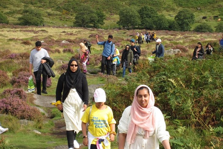 Asian families in a winding footpath in the countryside with ferns and purple heather in the foreground and trees and bushes in the background