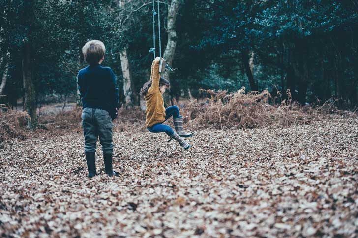 Children play on a swing in a wood with red leaves