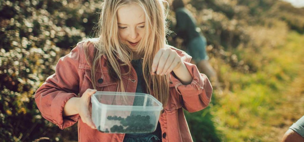 A teenage girl holds a Tupperware container with blackberries in