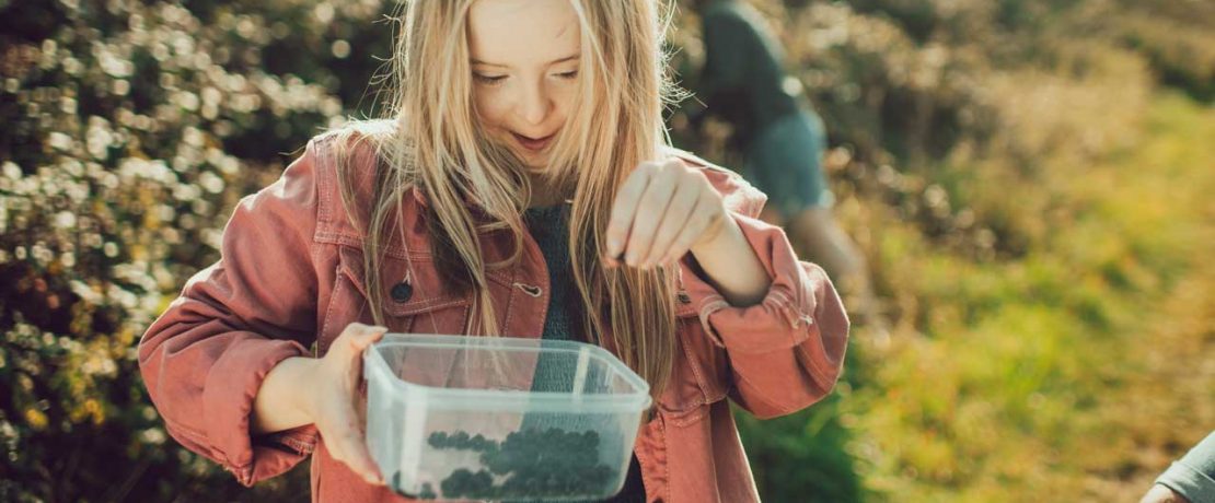 A teenage girl holds a Tupperware container with blackberries in