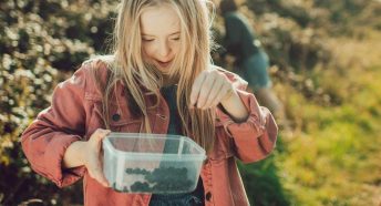 A teenage girl holds a Tupperware container with blackberries in
