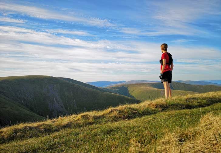 A man in running kit stands on a high fell looking over the hills