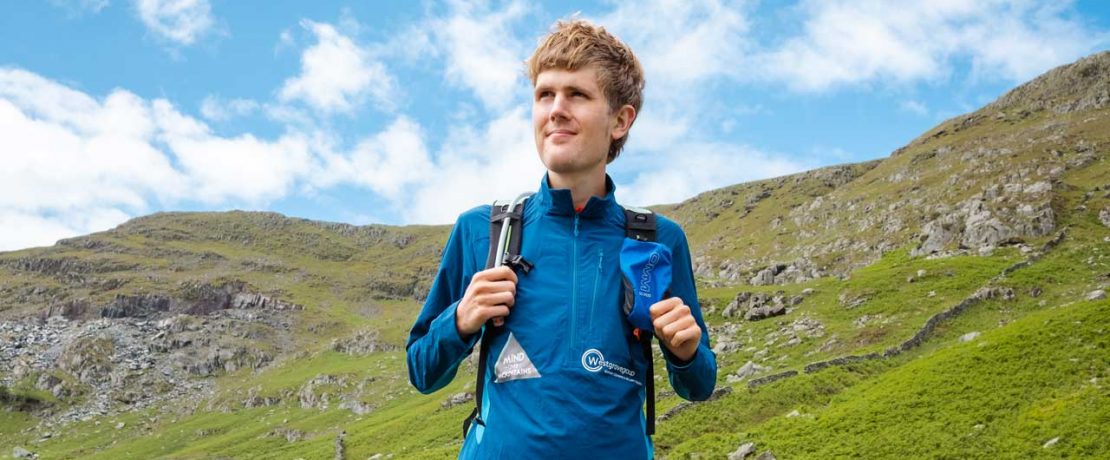 A man in outdoor clothing stands on a steep slope and looks out