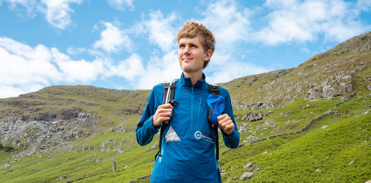 A man in outdoor clothing stands on a steep slope and looks out