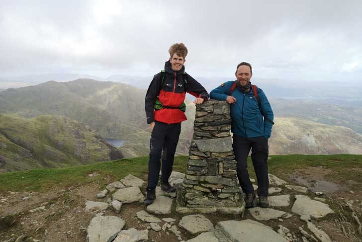 Two men beside a stony trig point on a hill top