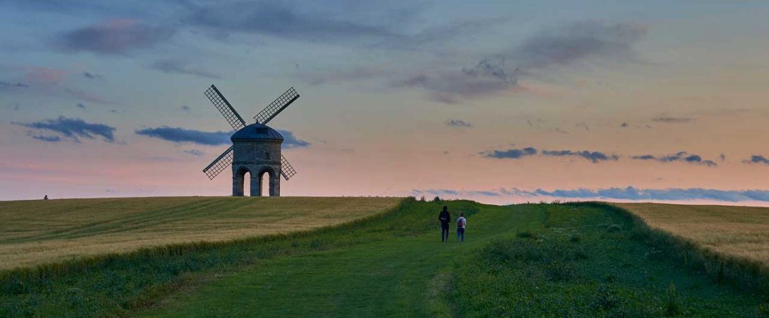 A windmill in a field with twilight sky behind and people walking nearby