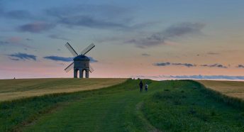 A windmill in a field with twilight sky behind and people walking nearby