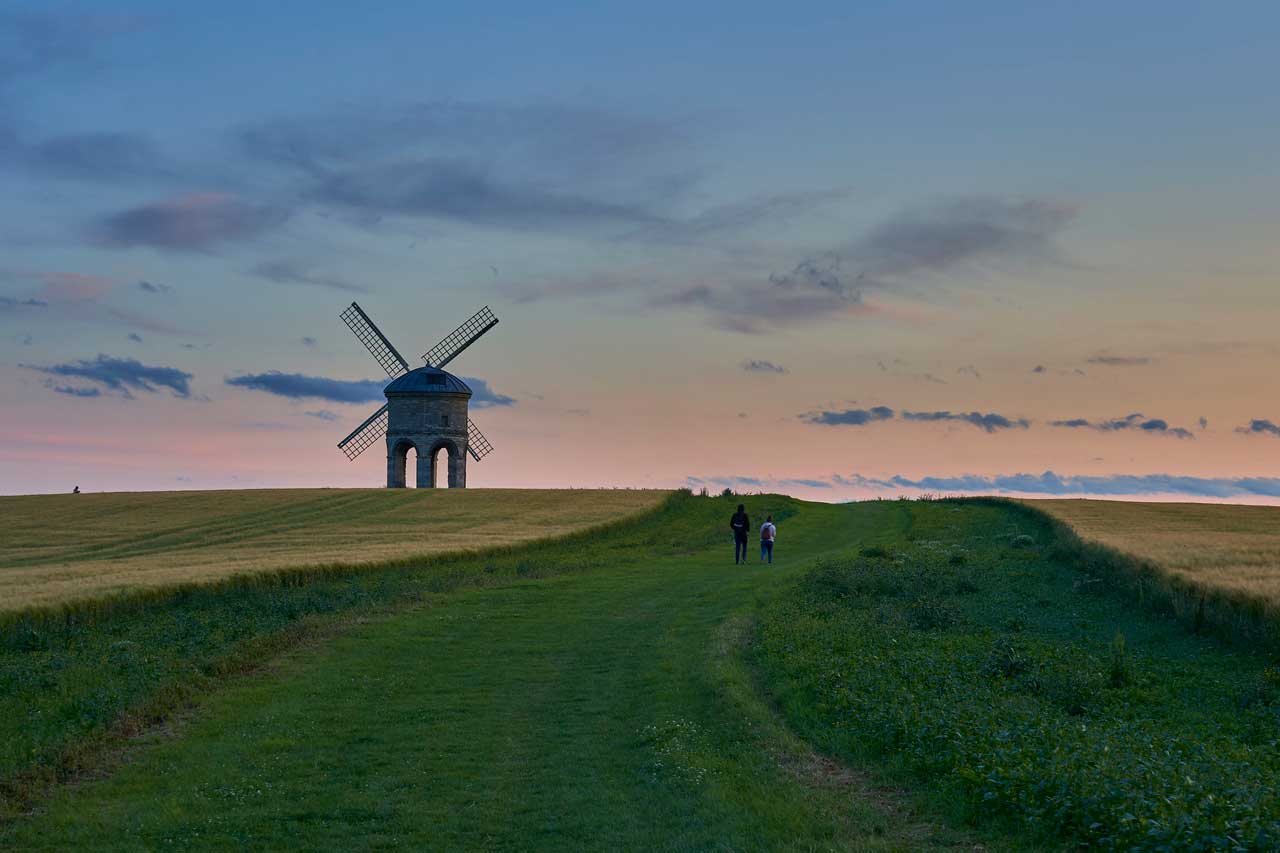 A windmill in a field with twilight sky behind and people walking nearby