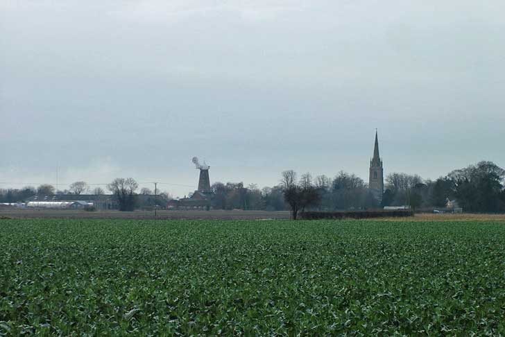 A windmill beyond a field with a church spire also visible