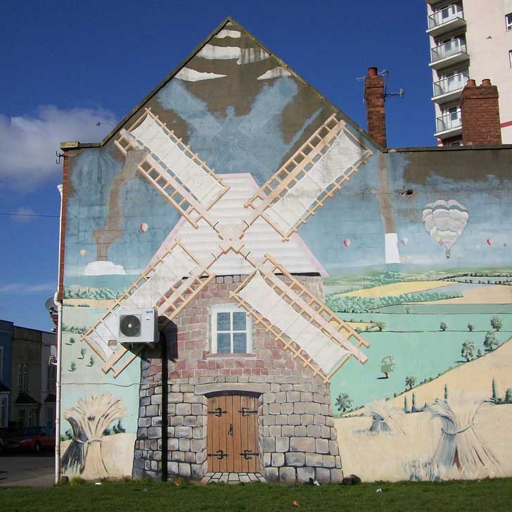 The side of a building with a painted windmill and rural scene