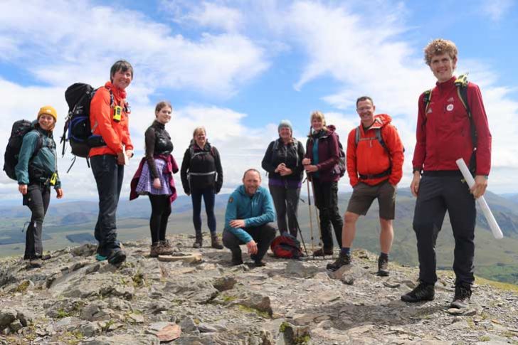 A group of people of various ages stand at the top of a hill