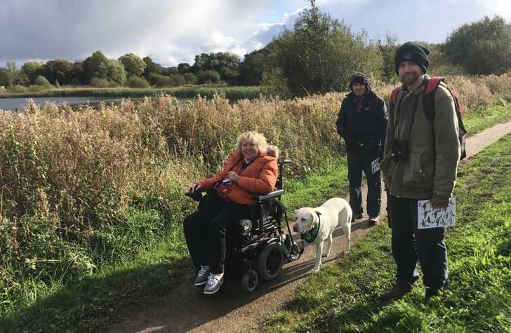 Three walkers, one using a wheelchair, and a dog on a grassy path