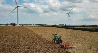 A tractor pulls a plough across a field with two win turbines behind
