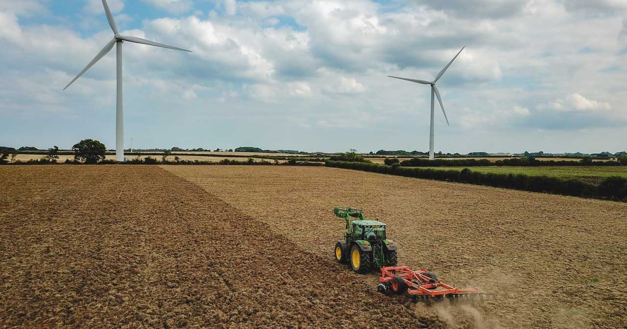 A tractor pulls a plough across a field with two win turbines behind