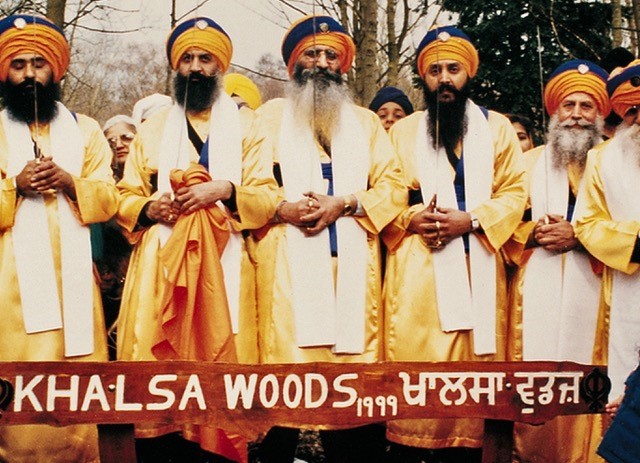A group of Sikh men in orange robes standing in front of a sign saying Khalsa Wood 199