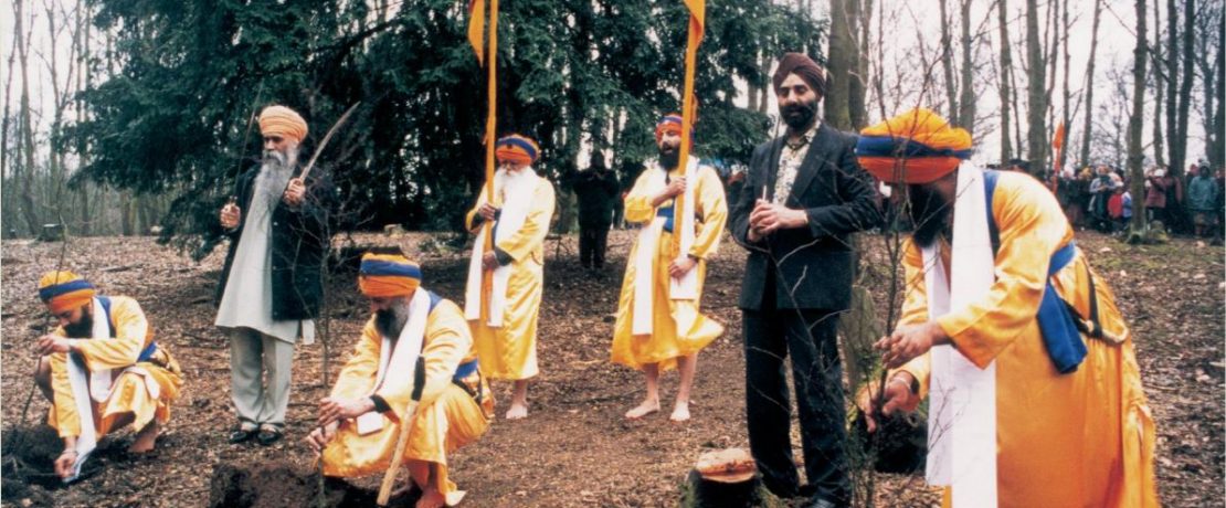 A group of Sikh men in orange robes planting trees in woodland