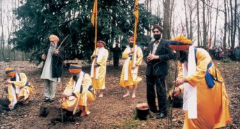 A group of Sikh men in orange robes planting trees in woodland