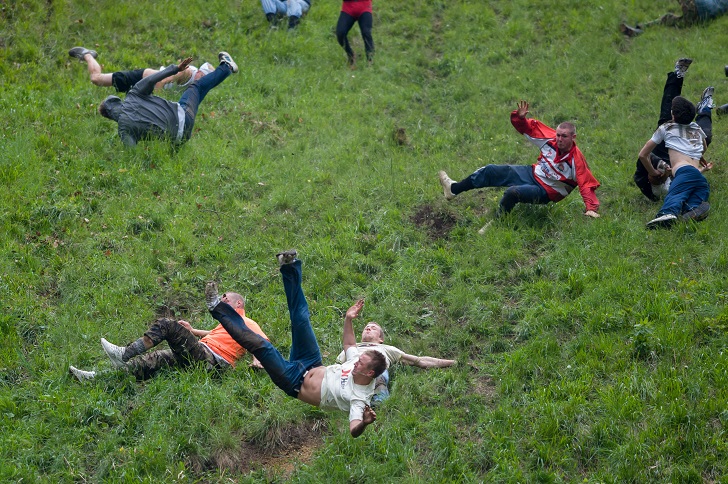 people rolling down a grassy hill