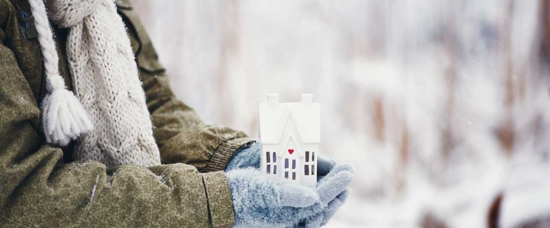 Gloved hands holding a small house in a snowy scene