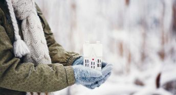 Gloved hands holding a small house in a snowy scene