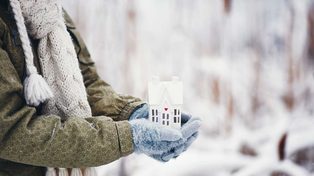 Gloved hands holding a small house in a snowy scene