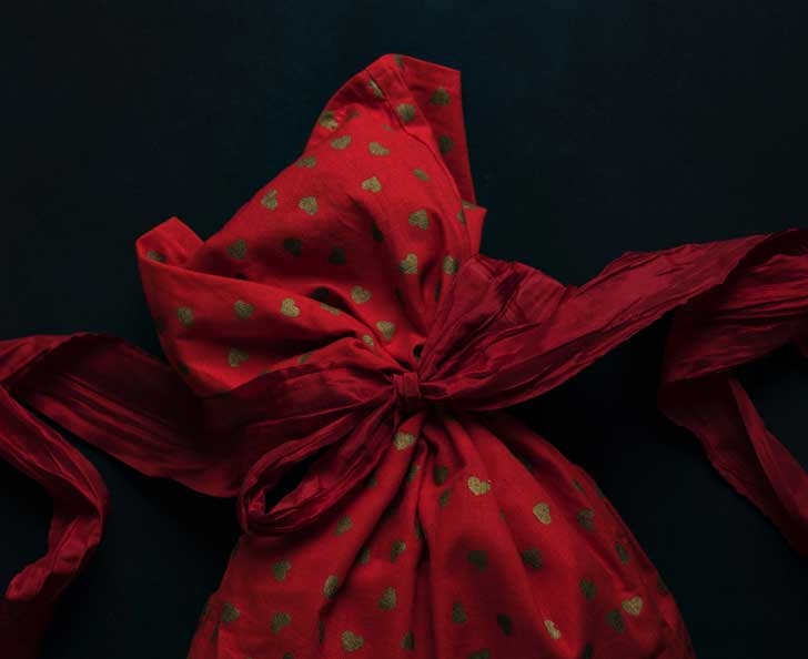 A gift wrapped in loose red and gold patterned fabric