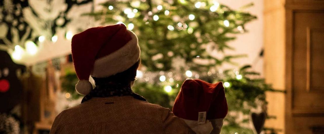 Two people in Santa hats look at a lit Christmas tree