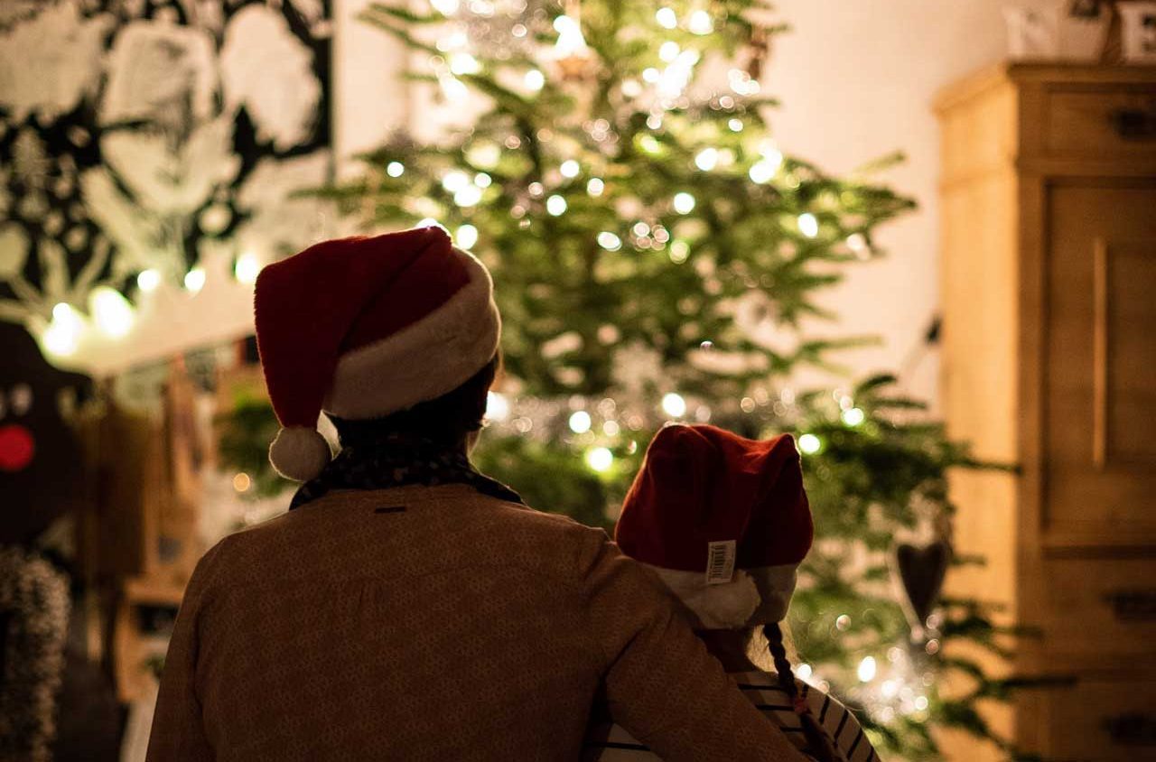 Two people in Santa hats look at a lit Christmas tree