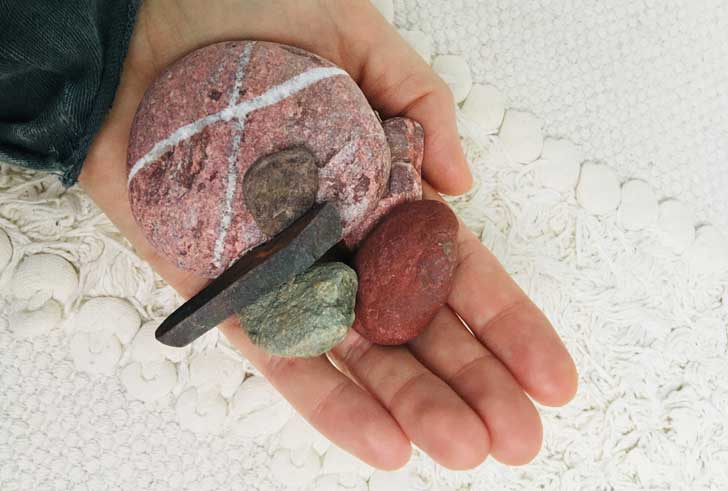 A hand holding pebbles in pinks and grey