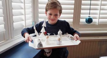 A small boy holds a tray with homemade figures and trees