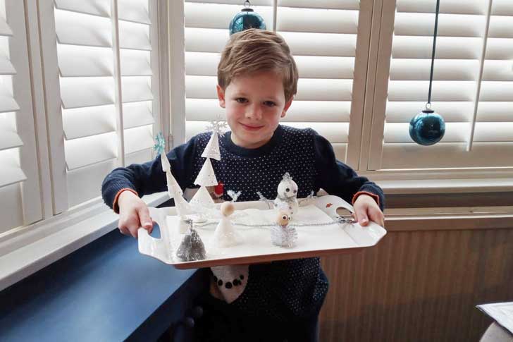 A small boy holds a tray with homemade figures and trees