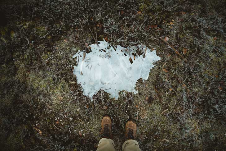 Hiking boots beside icy patch in the mud