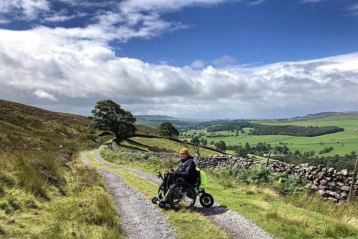 A man in a wheelchair on a dramatic countryside path